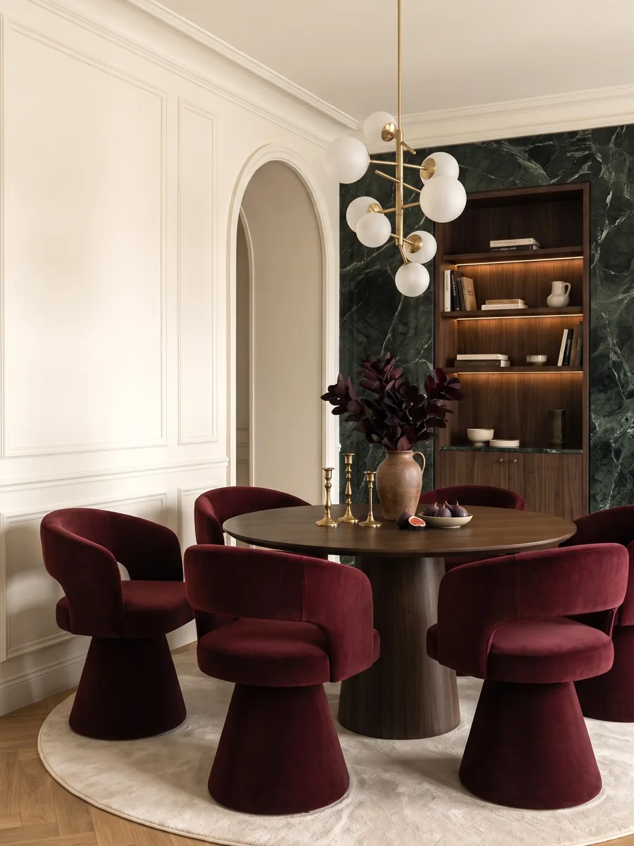 Dining area with burgundy velvet chairs, a round table, a dark green marble wall and a globe pendant